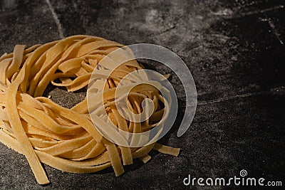 Isolated raw pasta on a black background with a place for text. Traditional Italian pasta, noodles, tagliatelle. Top view. Copy Stock Photo