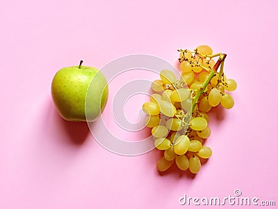 Isolated set of a green apple with a bunch of sweet seedless grapes in studio with millennial pink background Stock Photo