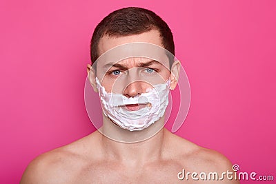 Isolated shot of handsome displeased European man has shaving gel on face, feels tired of everyday morning routine shows bare Stock Photo