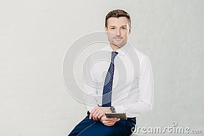 Isolated shot of successful male manager wears elegant white shirt, black trousers and tie, uses modern tablet computer for work a Stock Photo