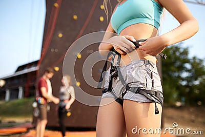 Isolated view of caucasian woman putting on belaying harness for practice on artificial rock wall outdoors. Slim strong Stock Photo