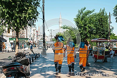 Istanbul, June 15, 2017: Three street janitors in bright orange uniforms are walking down the street holding brooms and Editorial Stock Photo