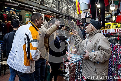 ISTANBUL, TURKEY - DECEMBER 28, 2015: Old merchant trying to sell anti stress head massage devices to laughing men near the spice Editorial Stock Photo