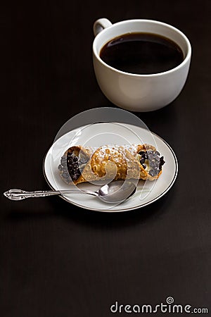 Italian cannoli with chocolate chips on white plate and coffee cup on black background Stock Photo