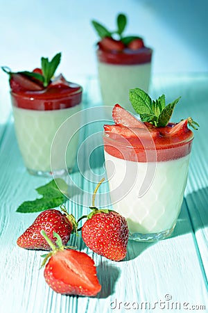 Italian dessert Panakota with strawberry coolies, fresh berries and mint on a blue background with hard shadows. Creamy milk Stock Photo