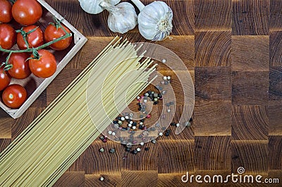 Cherry tomatoes, pasta spaghetti, garlic, and pepper on wooden brownn handmade cutting board Stock Photo