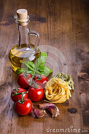 Italian and Mediterranean food ingredients on wooden background.Cherry tomatoes pasta, basil leaves and carafe with olive oil. Stock Photo