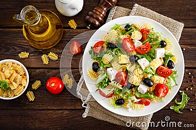 Italian pasta salad with fresh tomato, cheese, lettuce and olives on wooden background. Mediterranean cuisine. Cooking lunch. Hea Stock Photo