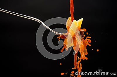 A drizzle of tomato sauce falls on a fork with the pasta creating many splashes on a black background Stock Photo