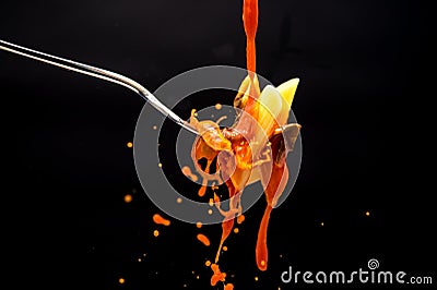 A drizzle of tomato sauce falls on a fork with the pasta creating many splashes on a black background Stock Photo
