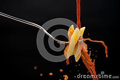 A drizzle of tomato sauce falls on a fork with the pasta creating many splashes on a black background Stock Photo