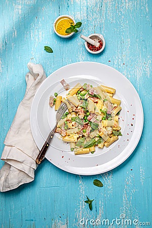 Italian recipe Pasta tortilloni with green pea, mint leaves, cheece, smoked bacon and cheese. Top view, blue background. Stock Photo