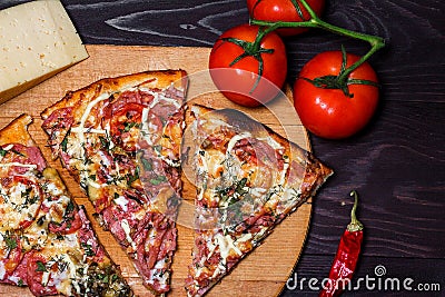 Italian rustic pizza, three pieces on a wooden tray, dark wooden table, with tomatoes, cheese and chili Stock Photo