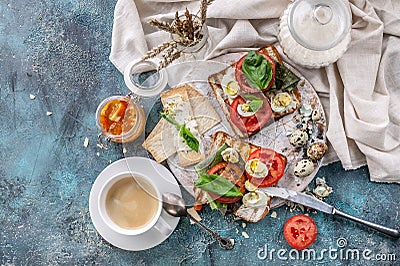 Italian toasts with cheese, tomatoes, basil, quail eggs and a cup of coffee. Ideas for a tasty and healthy breakfast. Top view Stock Photo