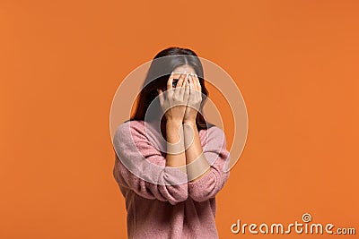 Its fear. Scared beautiful woman in pink sweater peeps through fingers, hides face with hands, looks terrified, afraids of Stock Photo