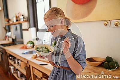 Its full of antioxidents. A young woman eating a bowl full of leafy greens in a rustic kitchen. Stock Photo