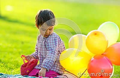 Ittle girl sitting on the grass with balloons in spring Stock Photo