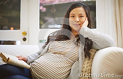 Ive got to take it easy before the baby arrives. Portrait of a pregnant woman reading a book at home. Stock Photo