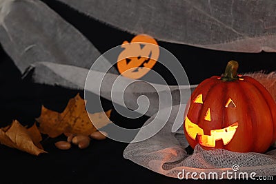 Jack pumpkin head on a dark background with gauze and decorations in the form of paper-cut bats and pumpkins. Burning candles. Stock Photo