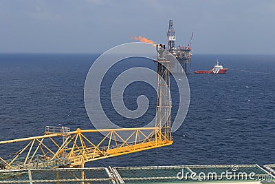 Jack up drilling rig, flare boom, and crew boat in the middle of Stock Photo