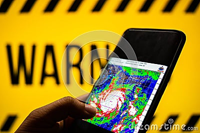 Mobile phone logged into photo of cyclone with warning background Editorial Stock Photo