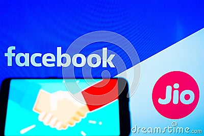 Mobile phone with a handshake screen and facebook and jio in the background Editorial Stock Photo