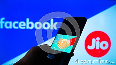 Mobile phone with a handshake screen and facebook and jio in the background Editorial Stock Photo