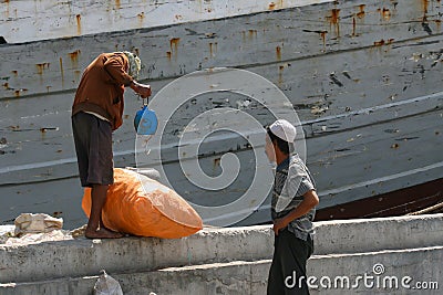 port workers weighing a sack in front of an old vessel Editorial Stock Photo