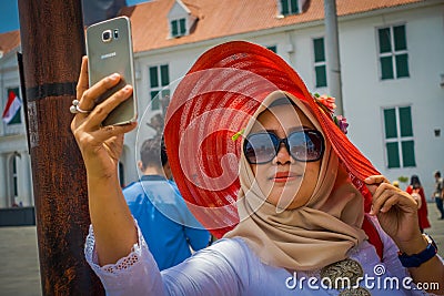 JAKARTA, INDONESIA - 3 MARCH, 2017: Local woman wearing large red hat takes a selfie while posing with sunglasses Editorial Stock Photo