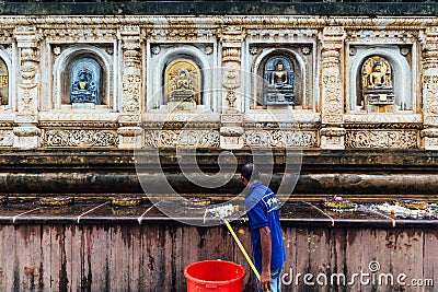 Janitor man cleaning wall of the temple that decorated with many forms and cultures of antique Buddha statues at Mahabodhi Temple. Editorial Stock Photo