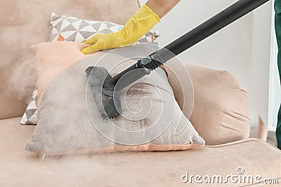 Janitor removing dirt from sofa cushion with steam cleaner Stock Photo