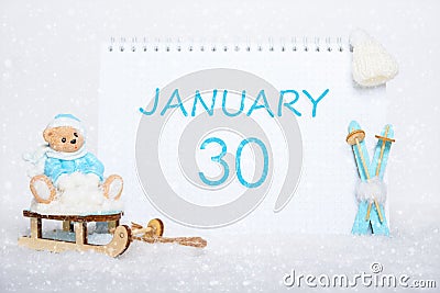 January 30th. Teddy bear sitting on a sled, blue skis and a calendar date on white snow. Day 30 of month. Stock Photo