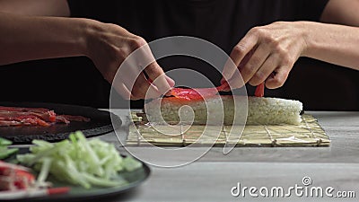 Japanese chef prepares sushi rolls with salmon and avocado. Cook hands making Japanese sushi roll on the bamboo mat Stock Photo