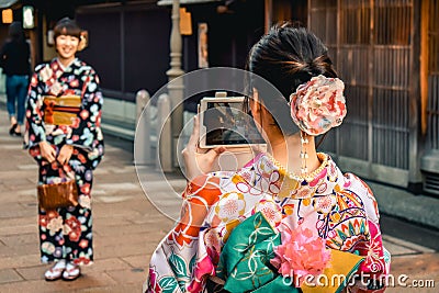 Japanese girls in Kimono`s taking photos of each other on a cell phone in the Kanazawa old town Editorial Stock Photo