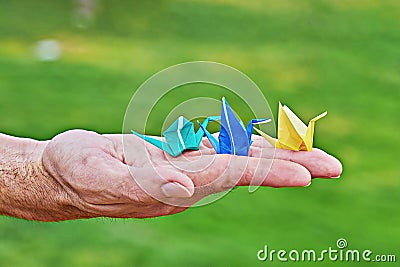 Japanese paper crane on male hand as symbol of happiness on green background Stock Photo