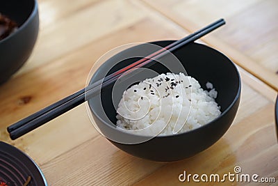 Japanese rice with black sesami on top in the black bowl and chopsticks on the wood table Stock Photo