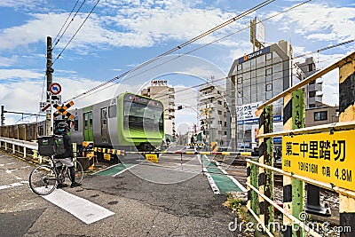 Japanese Uber Eats delivery man on bicycle waiting at a level crossing in Tokyo. Editorial Stock Photo