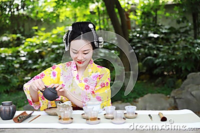 Traditional Asian Japanese beautiful Geisha woman wears kimono show tea art ceremony drink tea in a summer spring outdorr garden Stock Photo