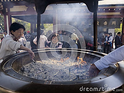 Japanese woman lights incense stick in the large bronze incense burner or koro at Senso-ji temple Editorial Stock Photo