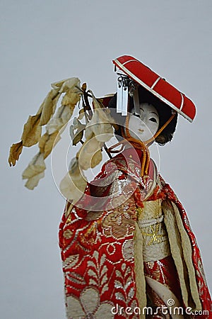 Japanese woman porcelain doll in red coat with decorative red hat and branch of broadleaved tree in hand Stock Photo