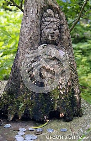 Japanese wood carving of a goddess with coins in a green forest Stock Photo