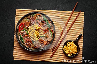 Japchae in black bowl on dark slate table top. Korean cuisine glass chapchae noodles dish with vegetables and meat Stock Photo