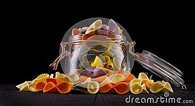 Jar of colorful farfalle pasta on wooden table isolated on black background Stock Photo