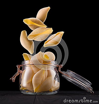 Jar of conchiglie pasta shell on wooden table isolated on black background Stock Photo