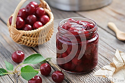 Jar of homemade cherry jam and basket of ripe cherries on table Stock Photo
