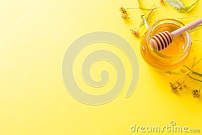 A jar of liquid honey from Linden flowers and a stick with honey on yellow background. Copy space Stock Photo