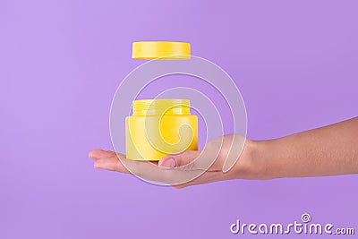 Jar of moisturizing facial cream. Yellow plastic container with cream vitamin c on purple background. Yellow unbranded, balsam, Stock Photo