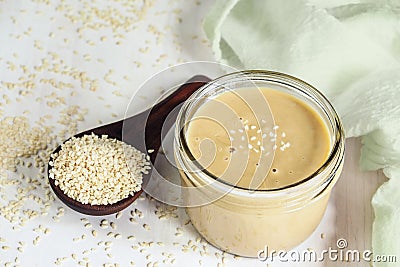 Jar of Tahini Sauce with Sesame Seeds in Wooden Spoon Stock Photo