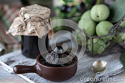 Jar of walnut jam on a wooden table and a group of green walnuts Stock Photo