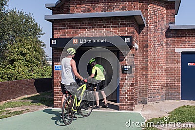 Cyclists waiting to enter lift to cycle tunnel outside on summers day Editorial Stock Photo